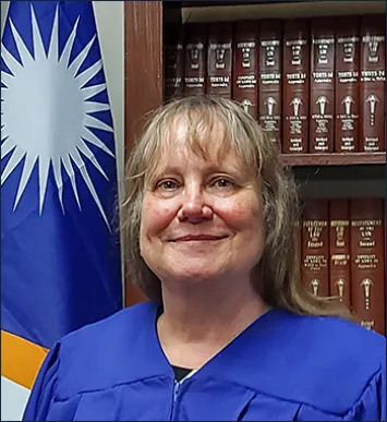 Middle-aged woman in judicial robe with books and flag background