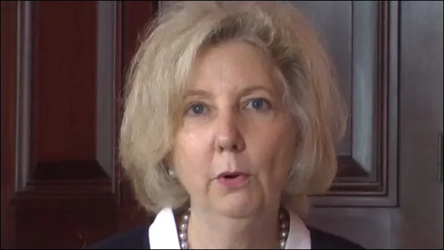 Close-up of a woman speaking in front of wood paneling
