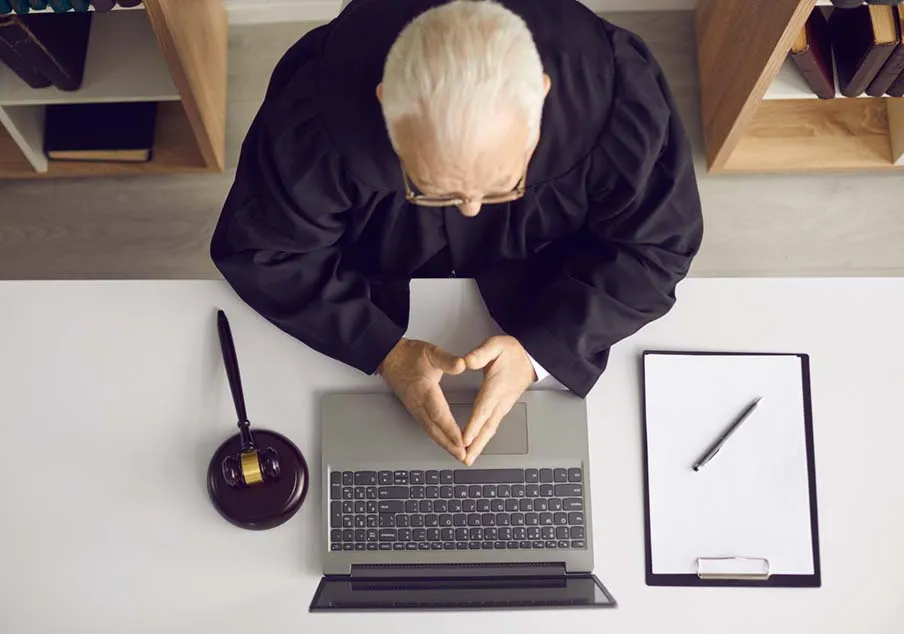 Judge in robe using laptop with gavel and clipboard